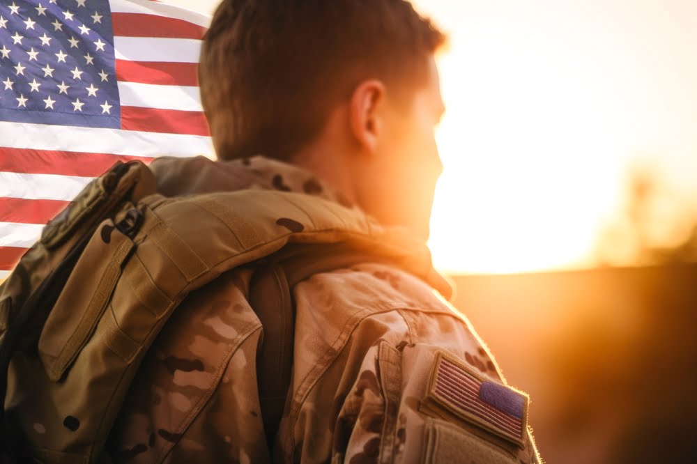 Rear view of a U.S. soldier looking at the sunset and a U.S. national flag